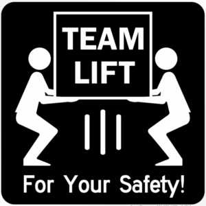 Sign with two people lifting a box with the saying, "Team Lift For Your Safety"